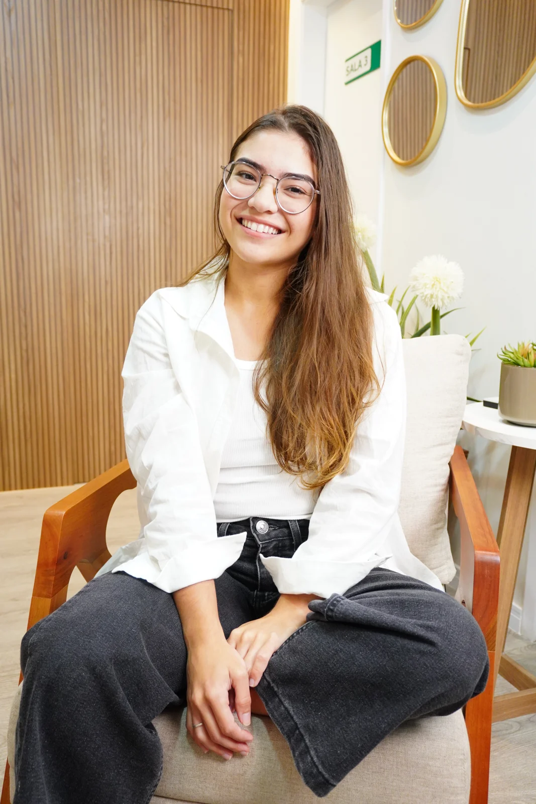 Maria Eduarda Sodré sentada no consultório, sorrindo para a câmera